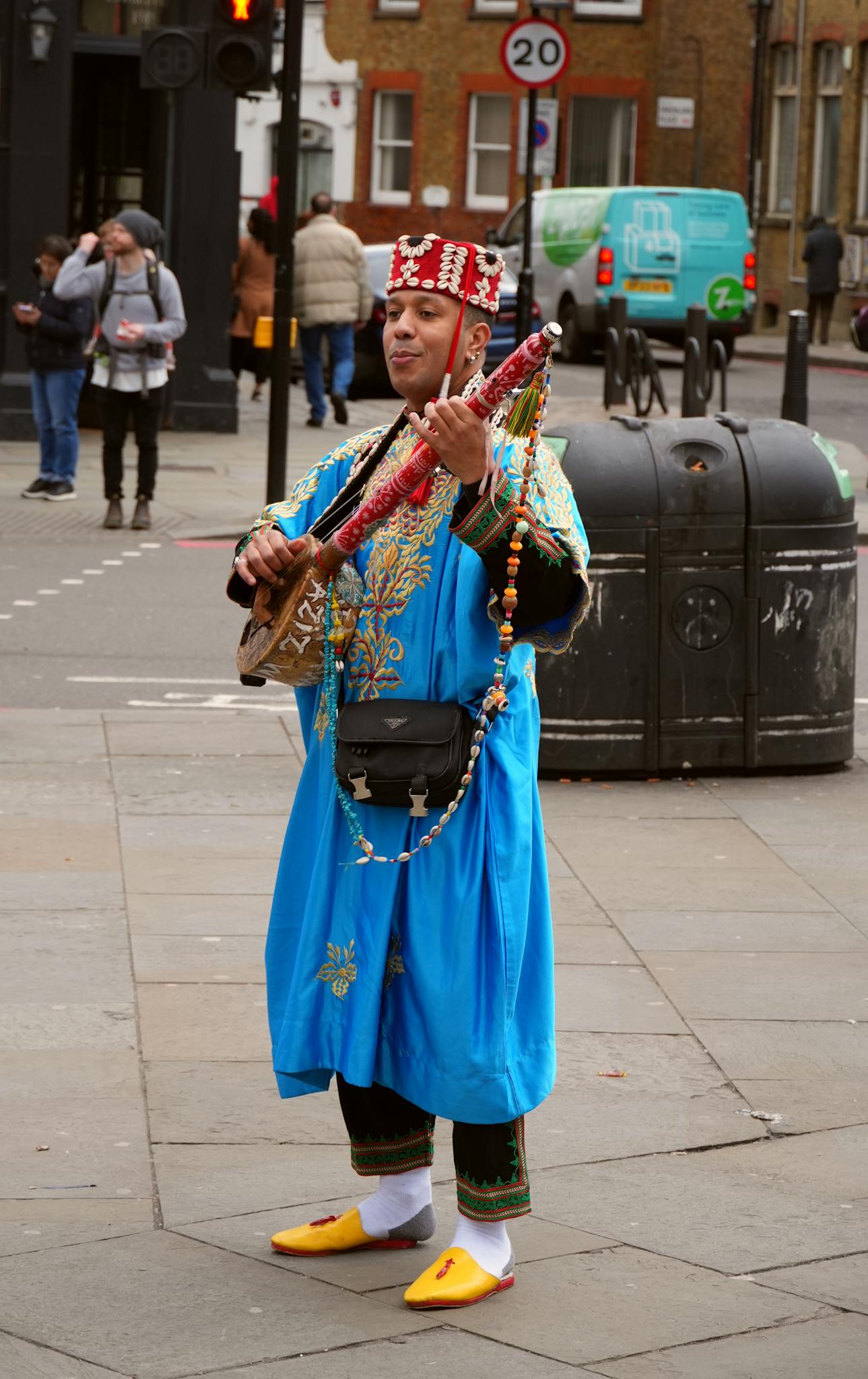 Moroccan musician in traditional clothing performing in urban England with a string instrument.